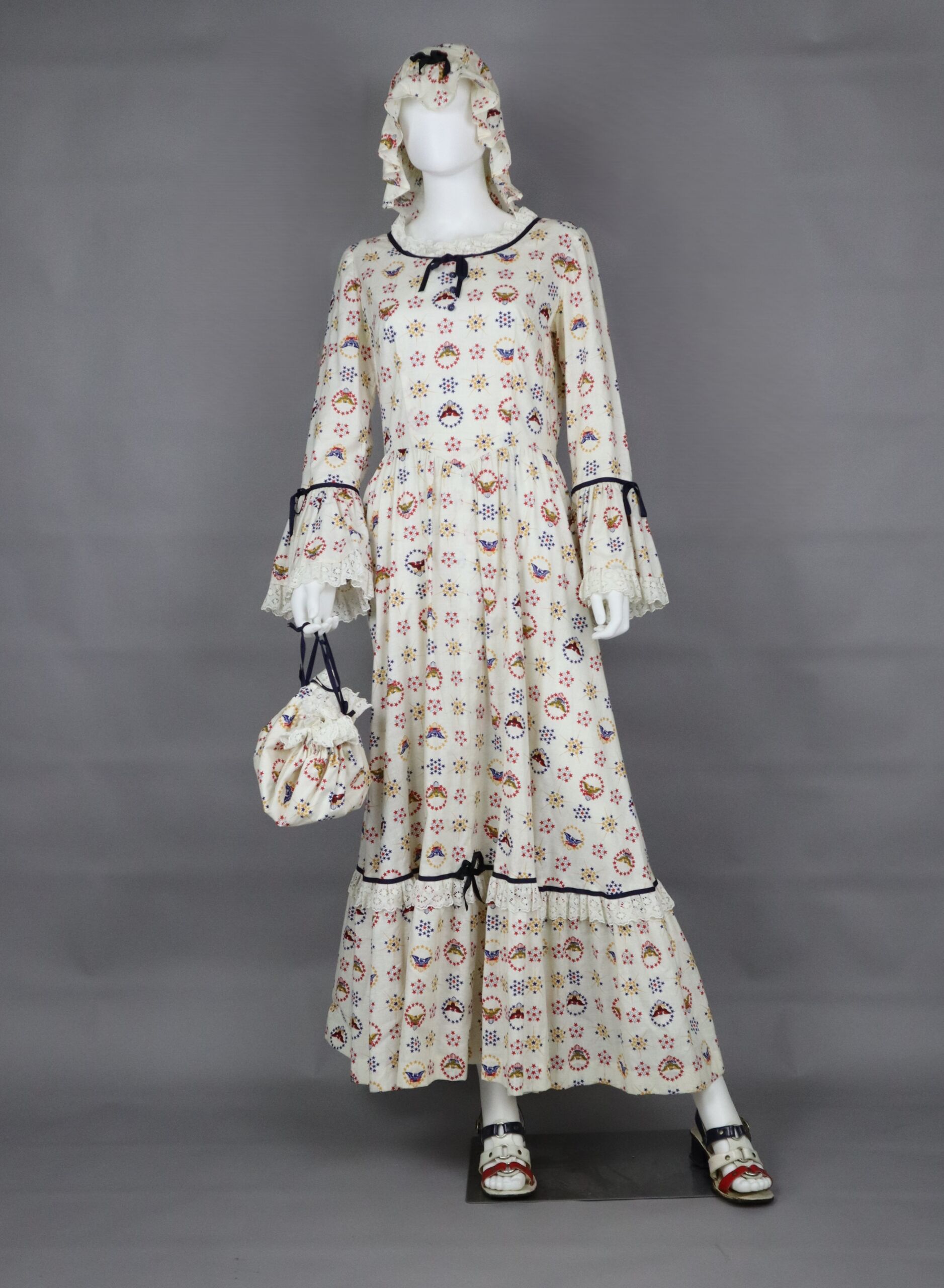Cream colored maxi dress covered in red, blue, and yellow stars and eagles, with matching bonnet and purse.